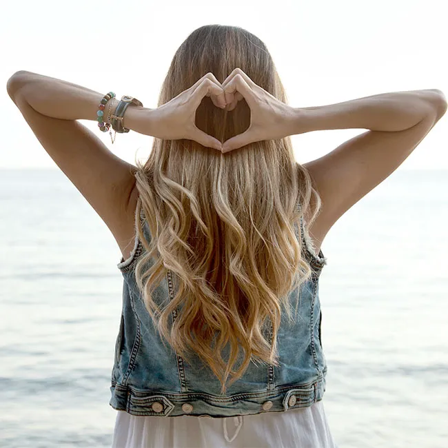 Wavy, healthy blonde hair styled in a heart shape with hands