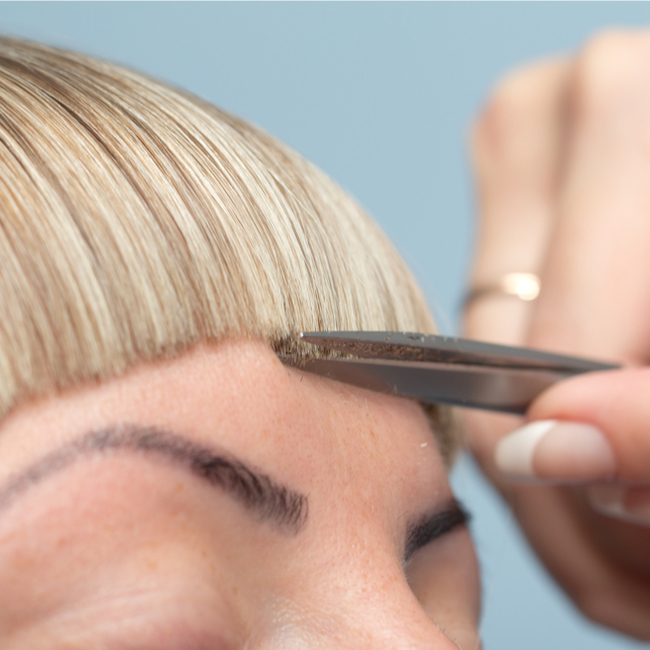 blonde hair blunt bangs scissors trim forehead above eyebrows salon