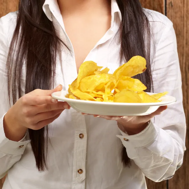 Woman enjoying a snack while holding a bag of chips.