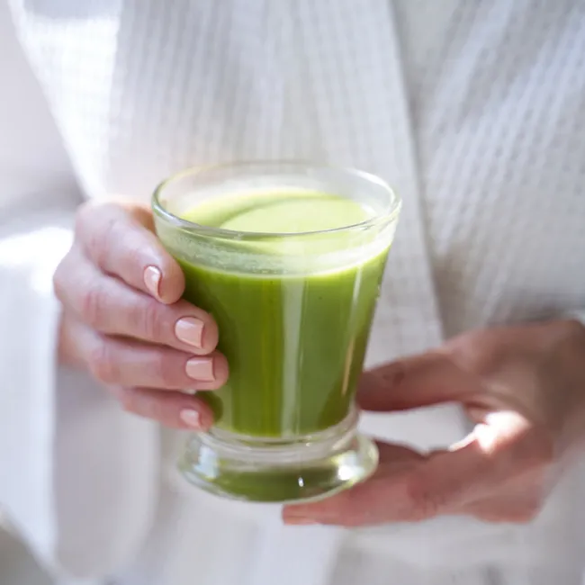 Person holding a vibrant green smoothie in a glass.