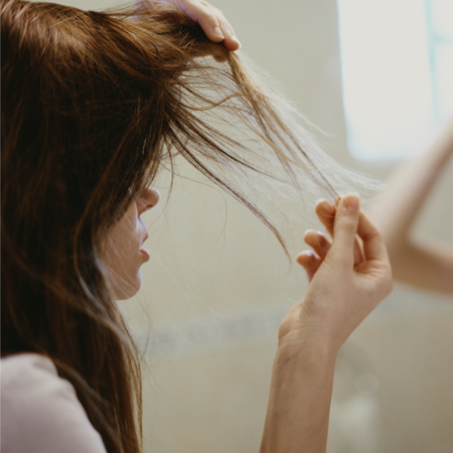 woman picking apart her thinning hair looking horrified in front of a mirror