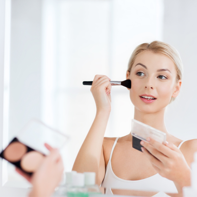 woman using highlighter and blush on her cheekbones powder