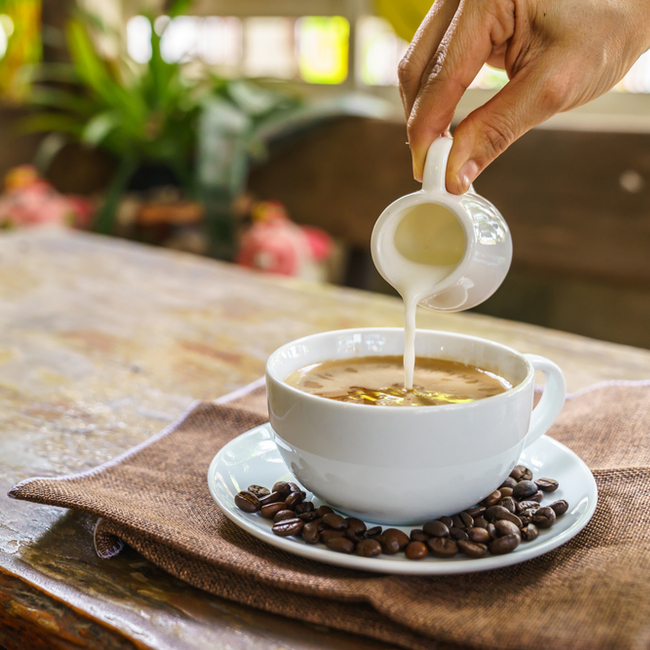 person pouring cream into cup of coffee