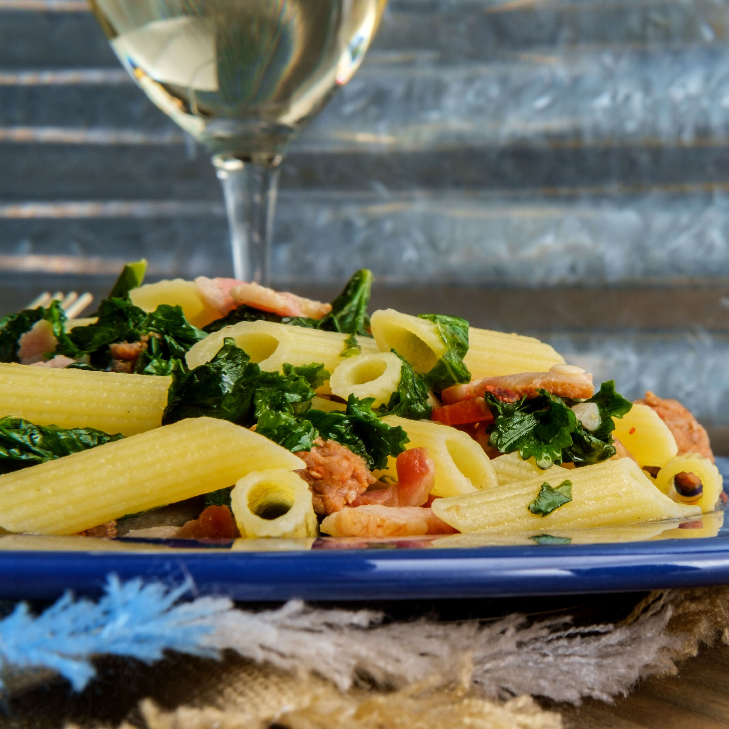 pasta with sausage and kale with glass of white wine in background