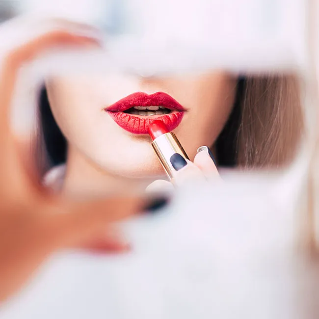 Applying red lipstick while looking in the mirror.