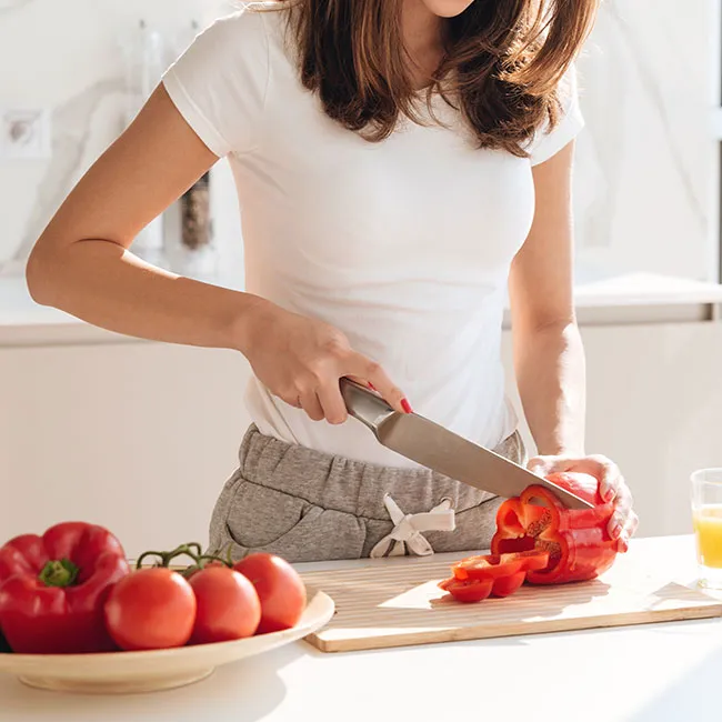 Woman chopping colorful peppers in a bright kitchen.