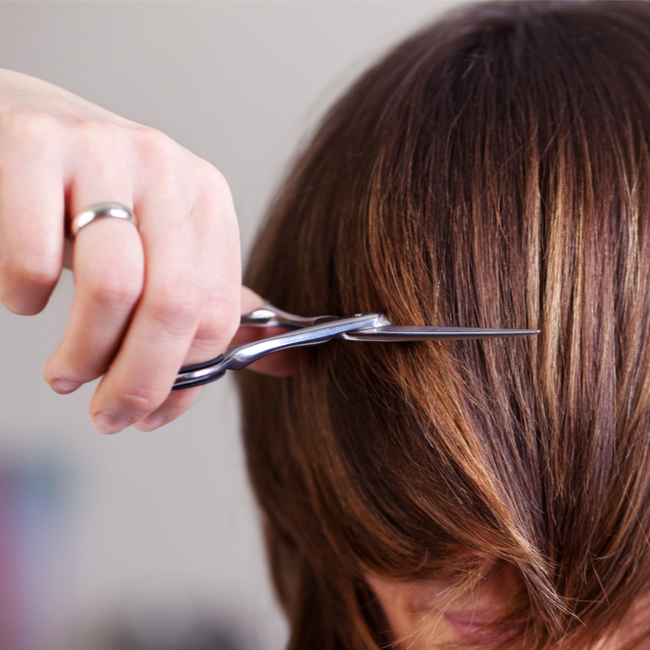 woman getting bang cut layers trim brown hair salon metal scissors stylist hand