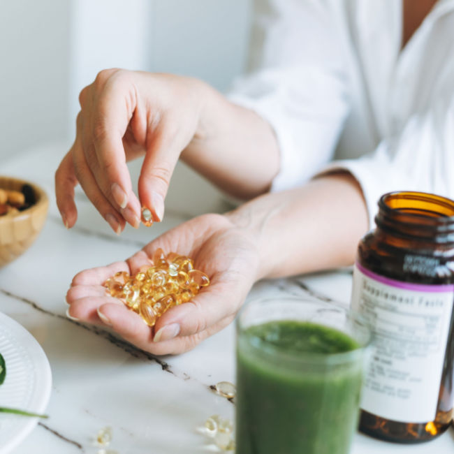 hand with supplements selecting one pill on table bottles nearby