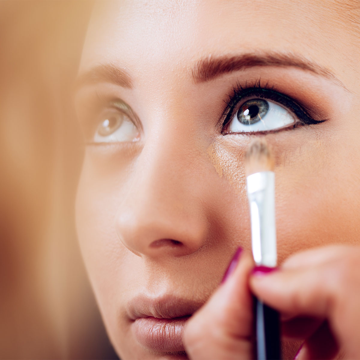 makeup artist applying concealer to model under-eye section
