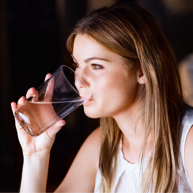 woman drinking water light straight brown hair white tank top