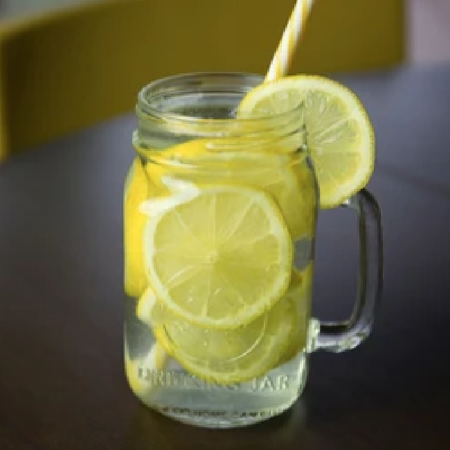 lemons and water in glass mug with paper straw on brown table