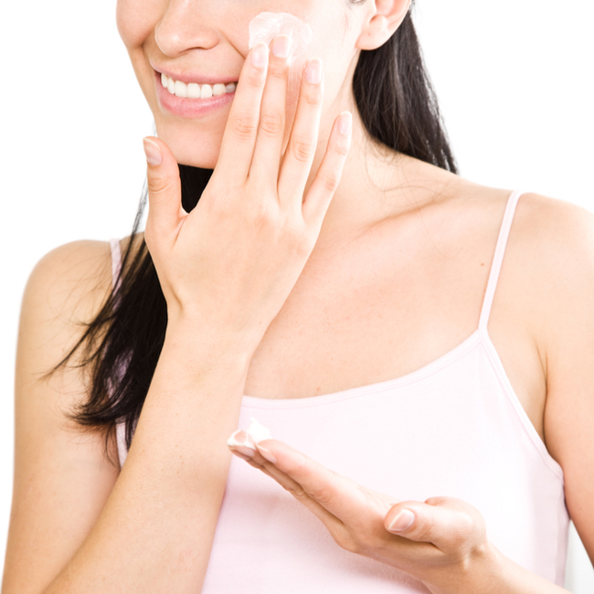 woman applying moisturizer with sunscreen to her face white tank top handds touching face