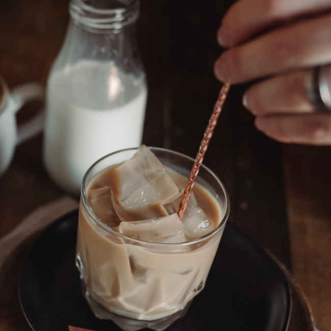stirring milk in iced coffee milk beside coffee on black table