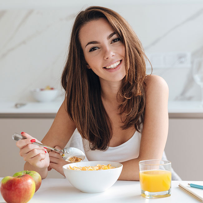 woman smiling eating healthy breakfast brown hair white table white bowl
