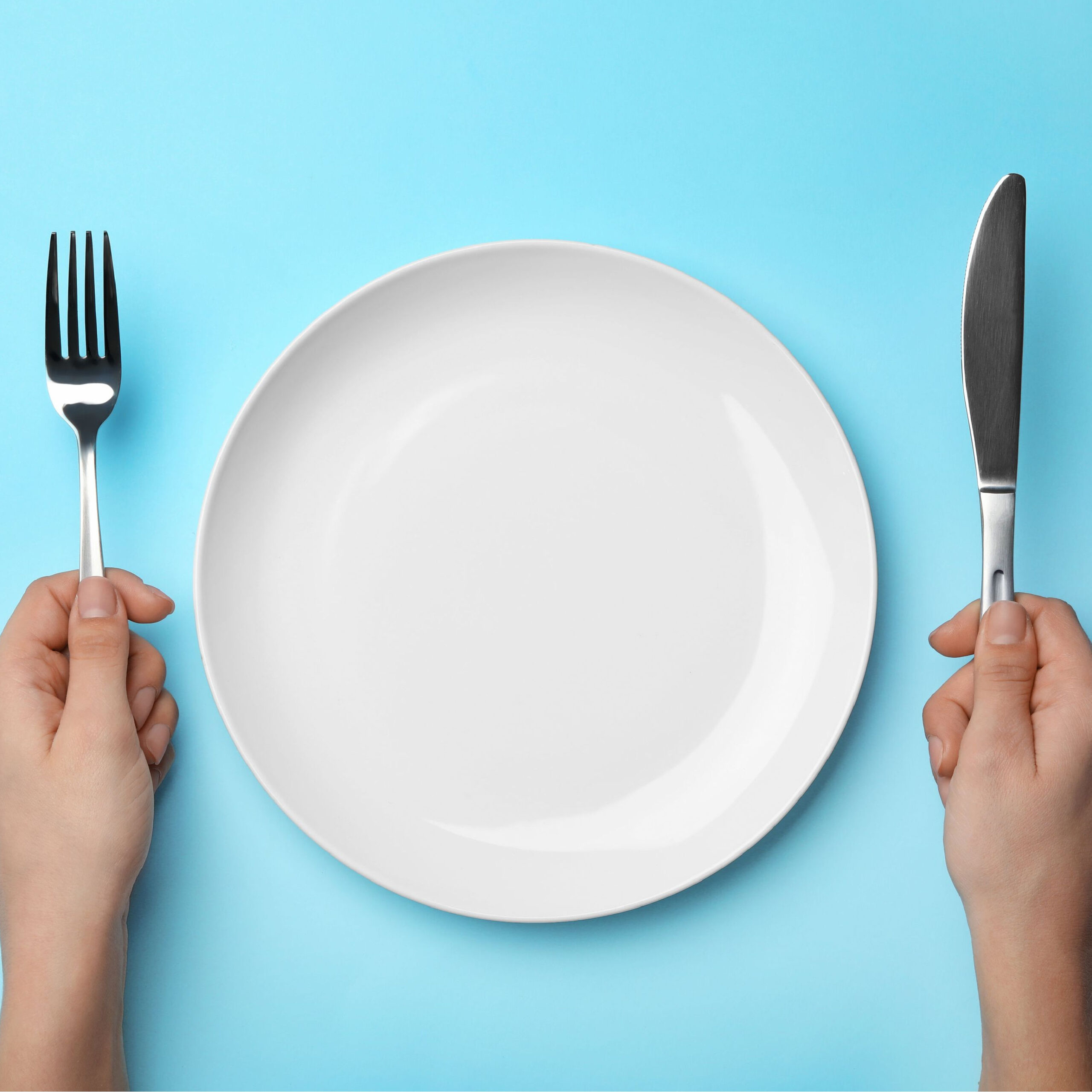 person holding fork and knife at an empty plate