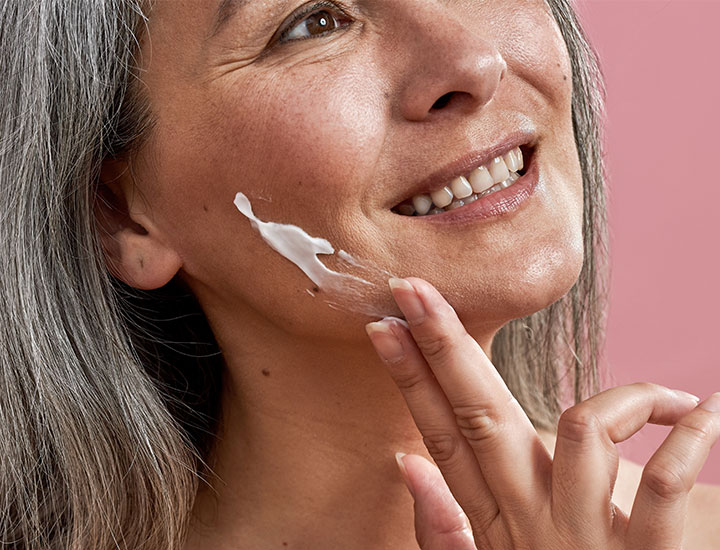 older woman applying sunscreen to cheek with fingers