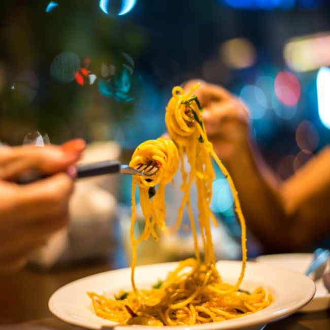 two people swirling spaghetti onto forks from a plate in a restaurant