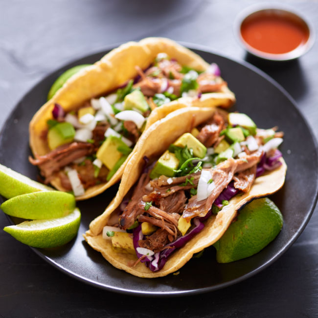 carnitas tacos topped with avocado, diced onions, and lime