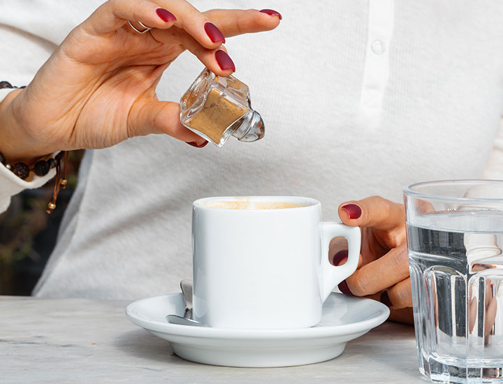 Woman adding cinnamon to coffee