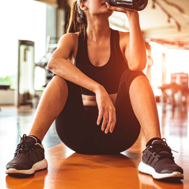 woman sitting on gym floor sipping water after workout
