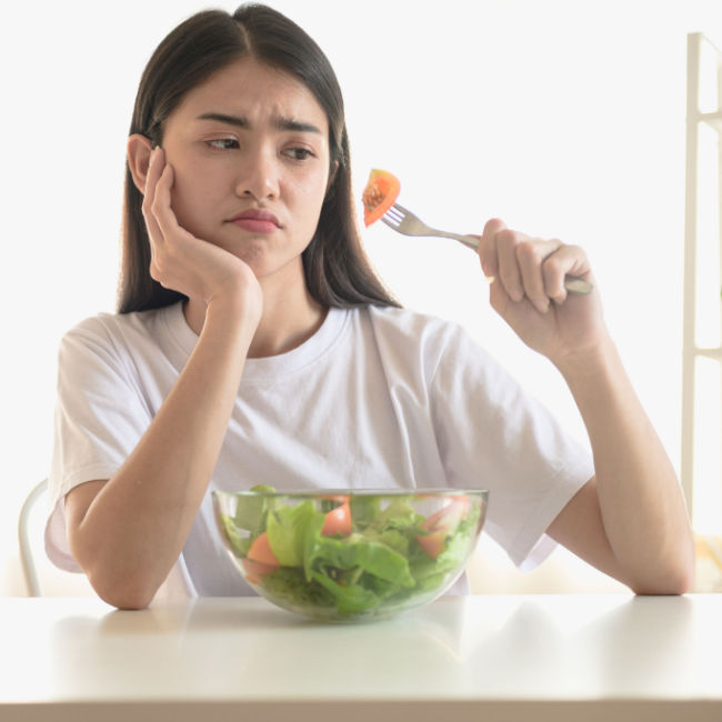 bored-looking woman picking at salad in kitchen
