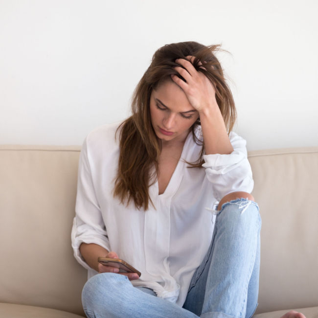 woman sitting on couch looking stressed out while looking at phone