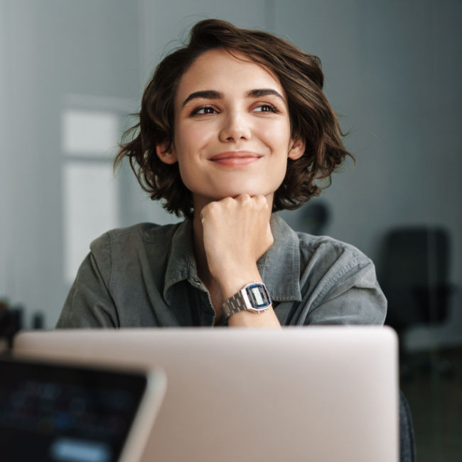 woman sitting in front of laptop and smiling optimistically with her chin on her hand
