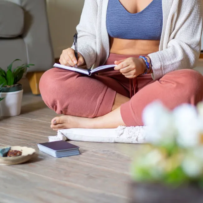 woman sitting and journaling on a pillow on the floor