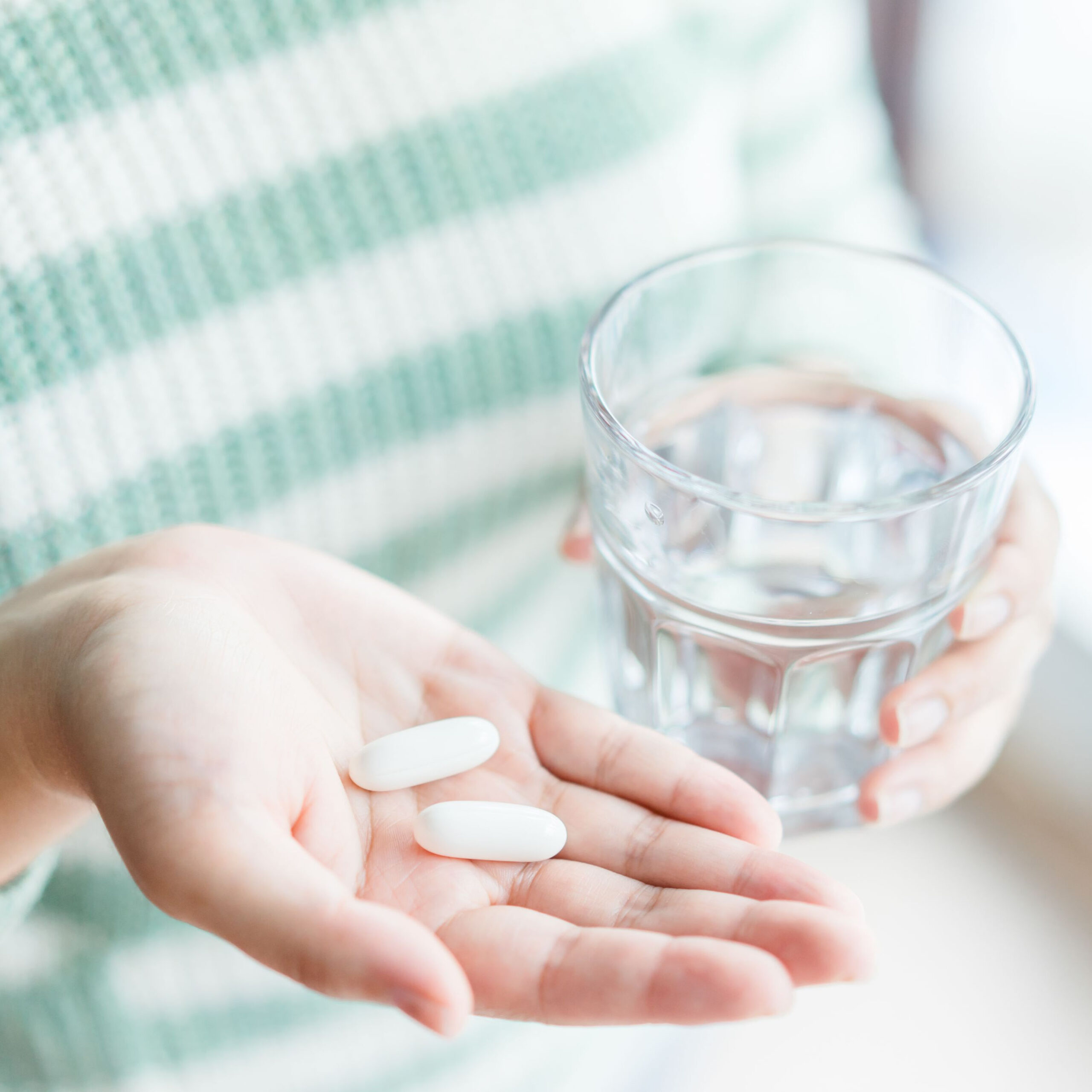 woman holding 2 vitamin d supplements and a glass of water