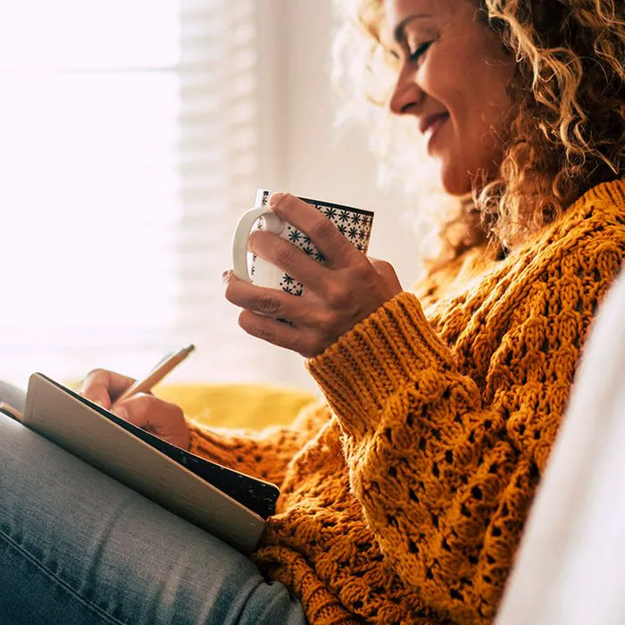 Cozy woman journaling while sipping tea.