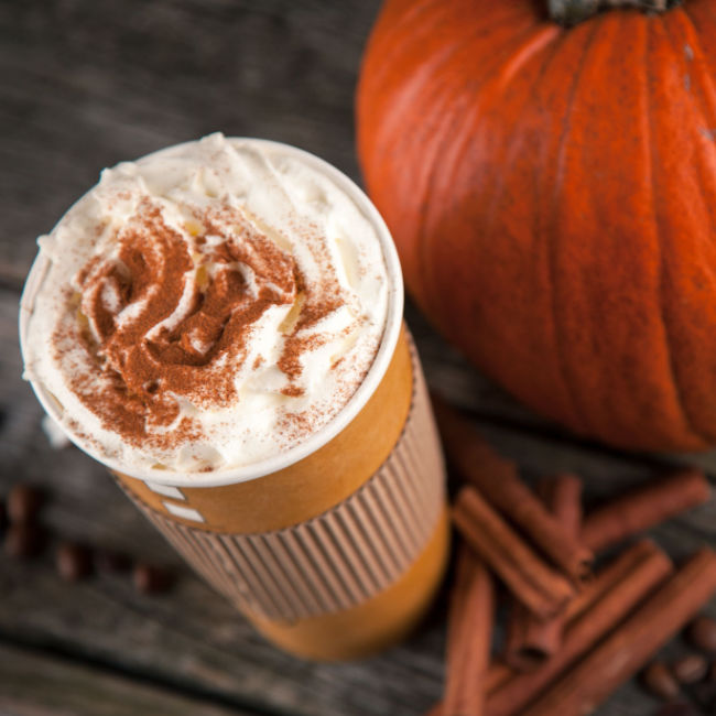 pumpkin spice latte with whipped cream in to-go cup next to pumpkin