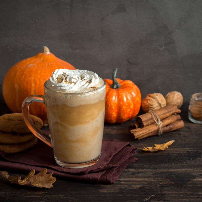pumpkin spice latte in glass mug with small pumpkins and cinnamon sticks on table