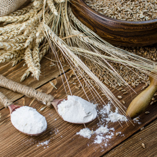 spoons of flower on wooden table beside wheat and grains