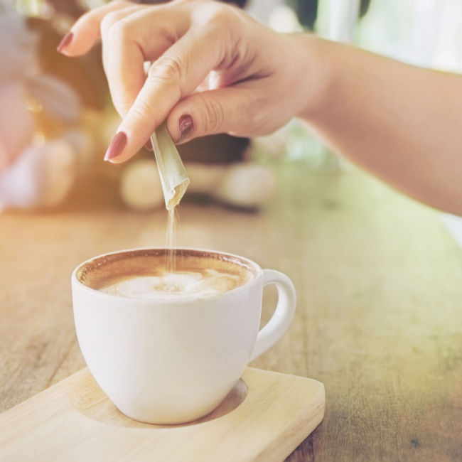 woman pouring sugar packet into coffee