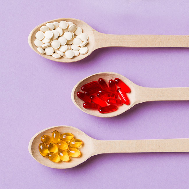supplements on wooden spoons purple background
