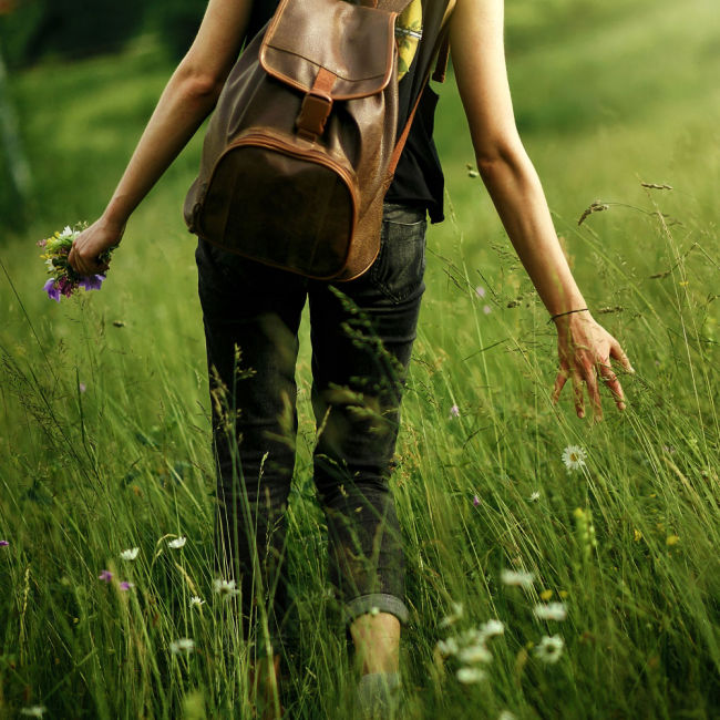 woman with backpack walking through meadow