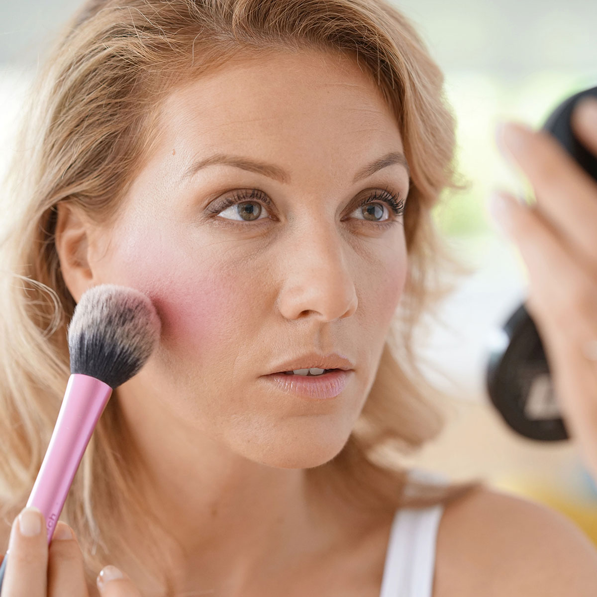 woman fanning out blush on cheekbones with powder brush