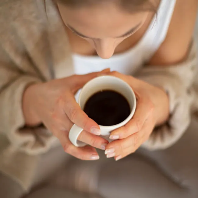 Woman enjoying a cup of black coffee in a cozy setting.