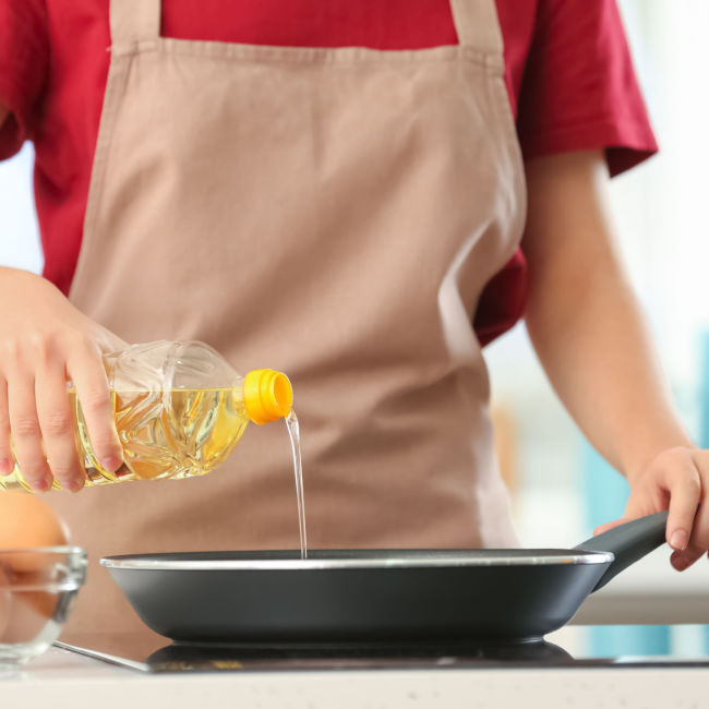 woman with apron on pouring cooking oil into pan