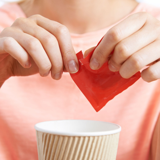 woman emptying sweetener packet into coffee