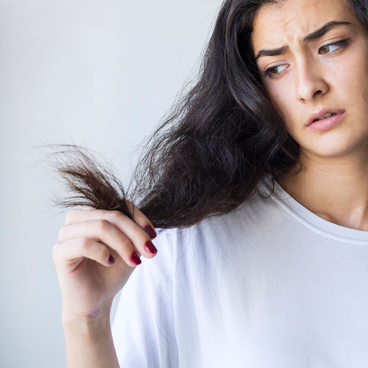woman looking upset while holding split ends frizzy brown hair