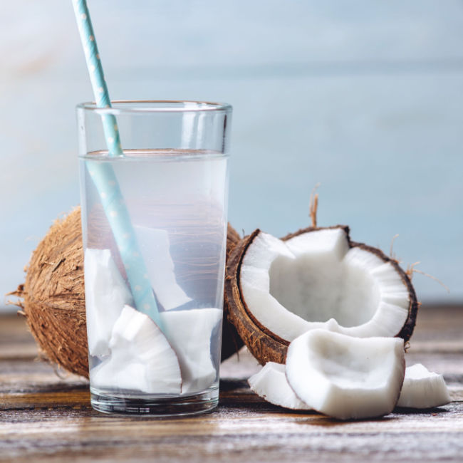 coconut water in glass with straw in front of open coocnut