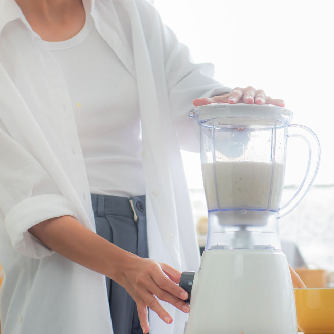 woman wearing white blending a smoothie in kitchen