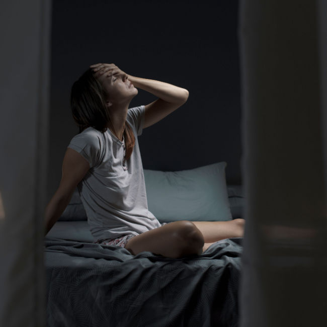 woman sitting up in bed too hot to sleep