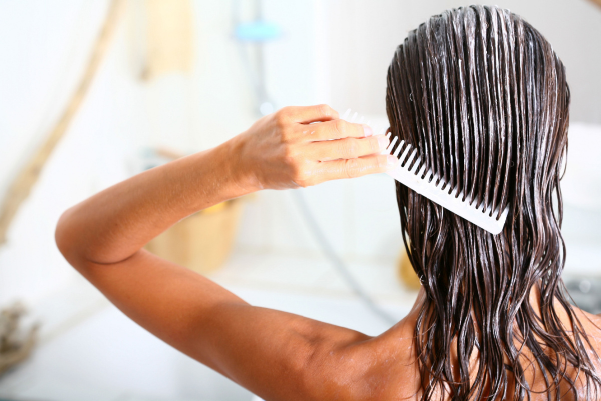Woman brushing conditioner through her hair.