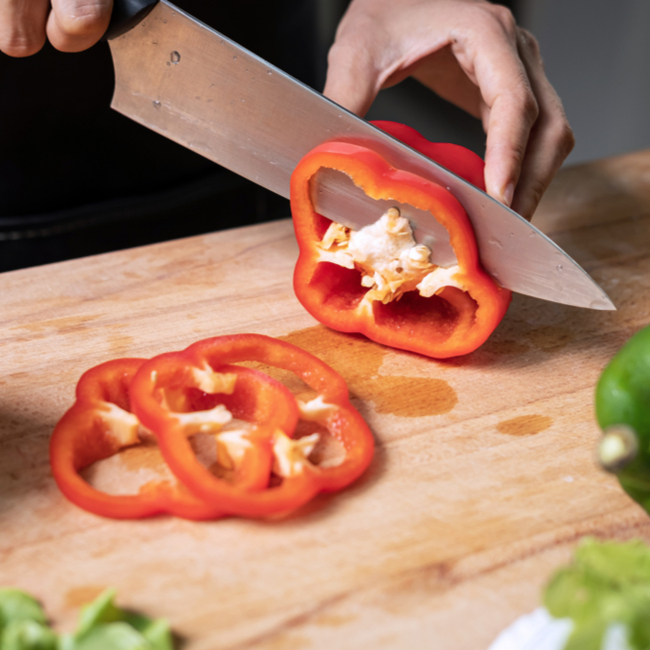 person slicing red bell pepper in kitchen