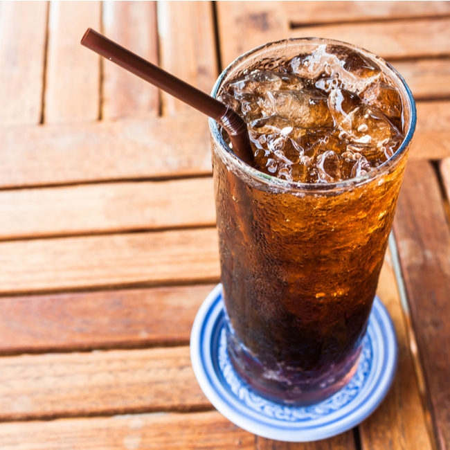 glass of cola with straw on wooden table