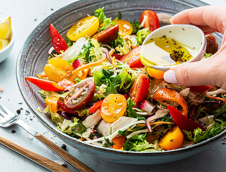 Person pouring dressing on a salad.