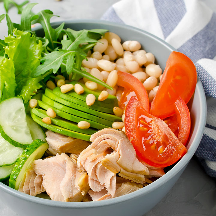 healthy salad bowl of white beans, avocado, cucumber, tomato, pine nuts, and meat