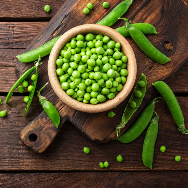 bowl of green peas surrounded by pea pods
